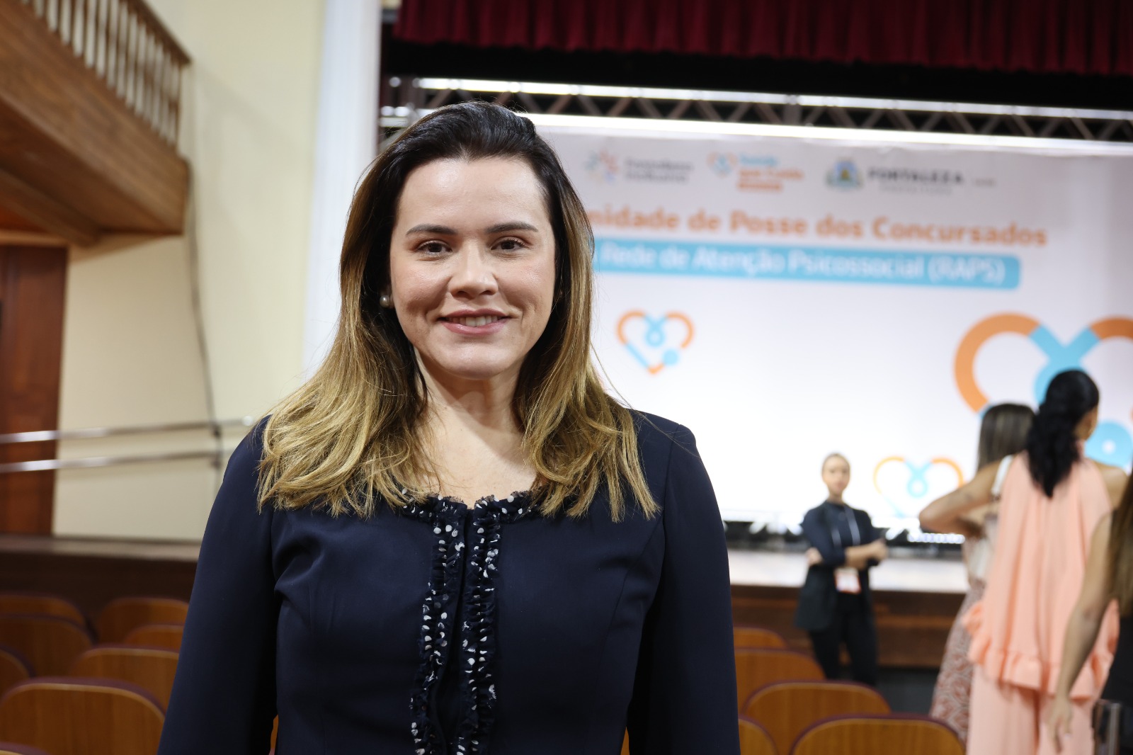 Renata Pinheiro posa para a foto, ela é branca, tem cabelo castanho comprido e usa blusa preta